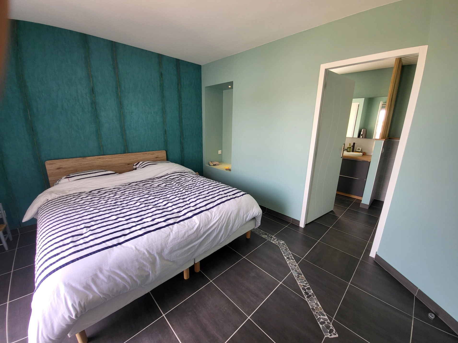 Suite parentale avec grand lit au centre, murs verts et salle de bain attenante
